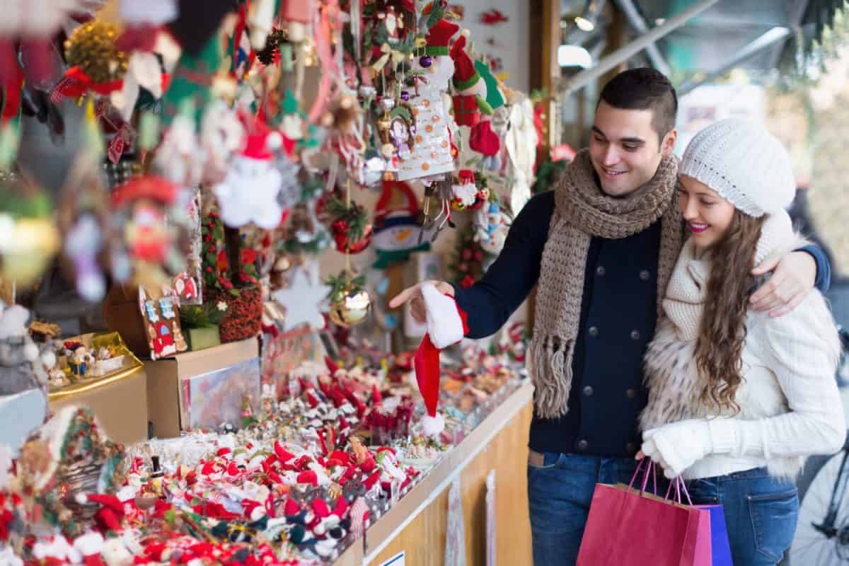 Smiling young girl with boyfriend choosing Christmas decoration at fair. Focus on man