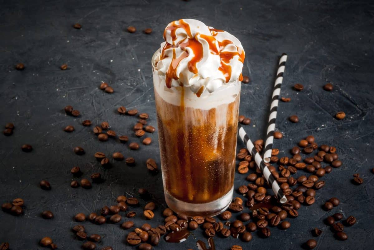 Cold coffee drink frappe (frappuccino), with whipped cream and caramel syrup, with straws and grains of coffee on a dark gray stone table, copy space