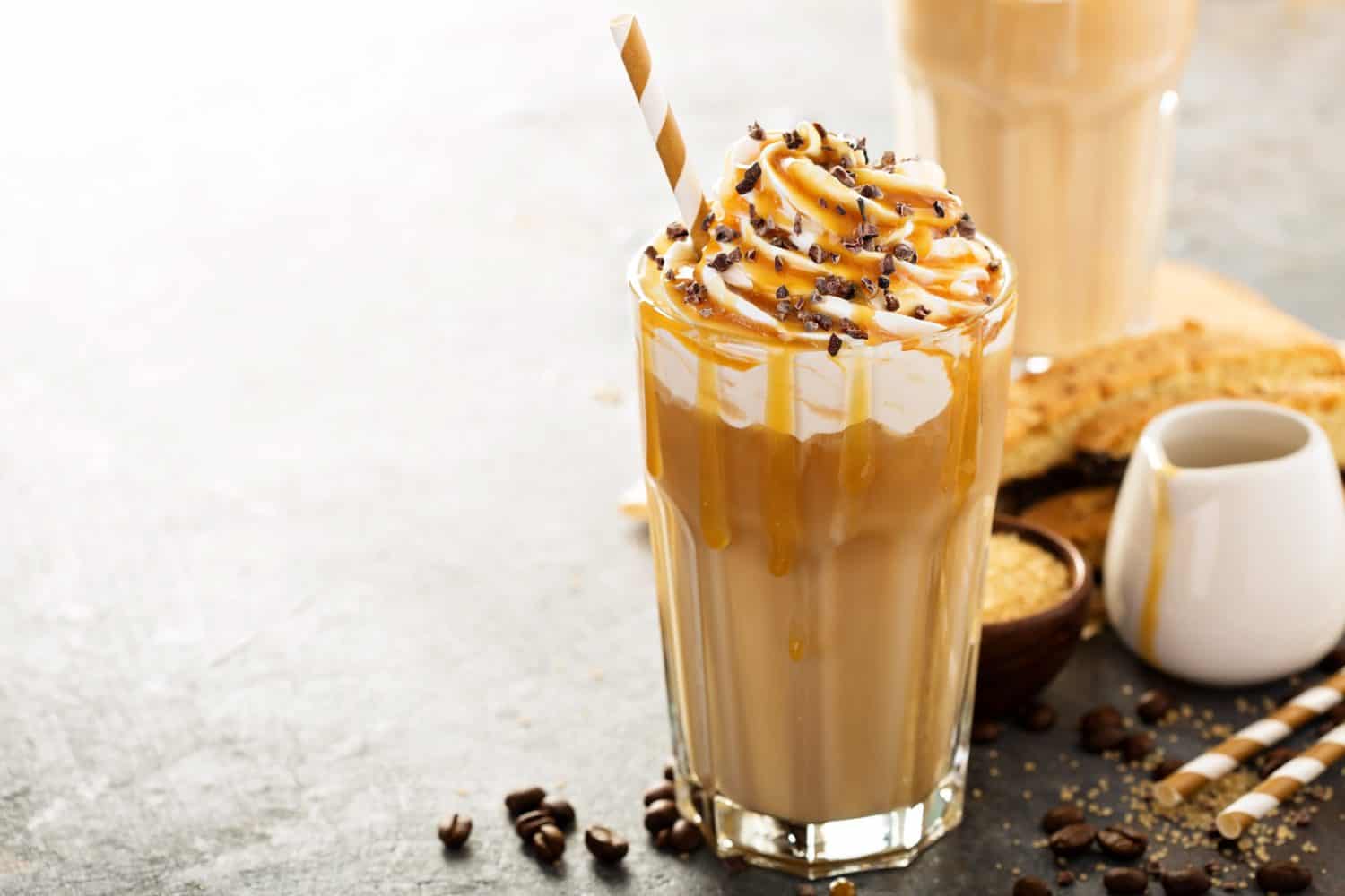 Iced caramel latte coffee in a tall glass with syrup and whipped cream.