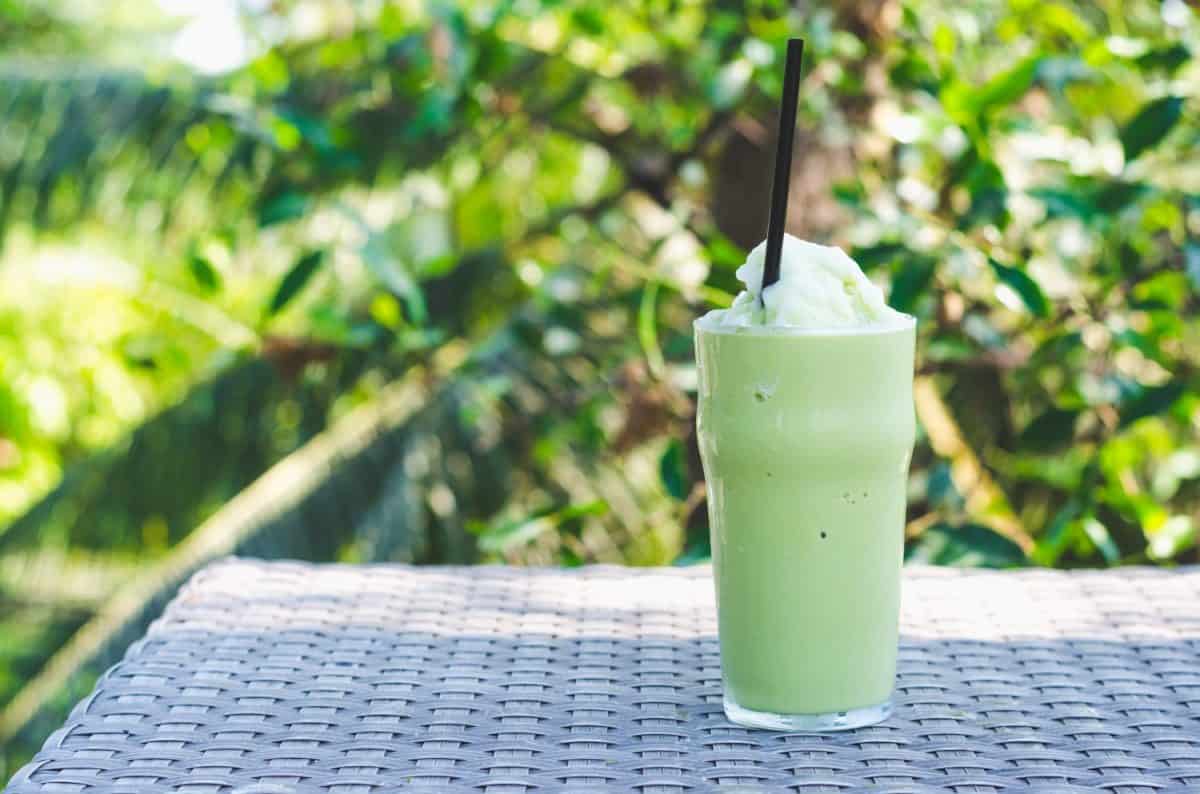 glass of green tea frappe , ice shake with green plant background.