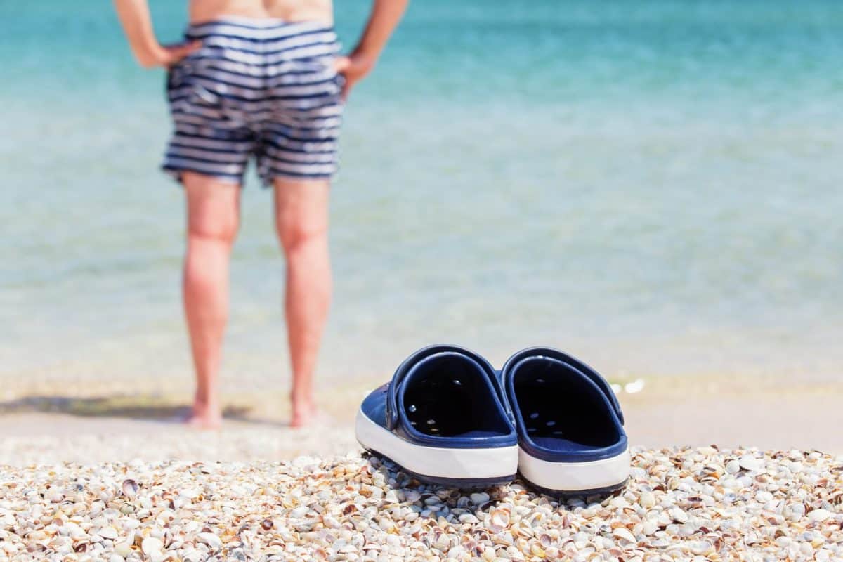 Sandals, clogs on the shell seaside. Against a background, a person in swimming trunks goes into the water. Forget Crocs, Here's 8 Better Options for Your Feet