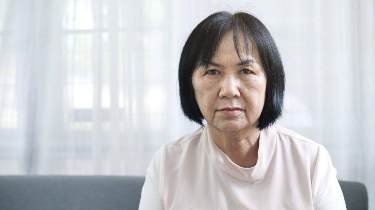 Face of unhappy lonely Asian senior woman sitting alone at home