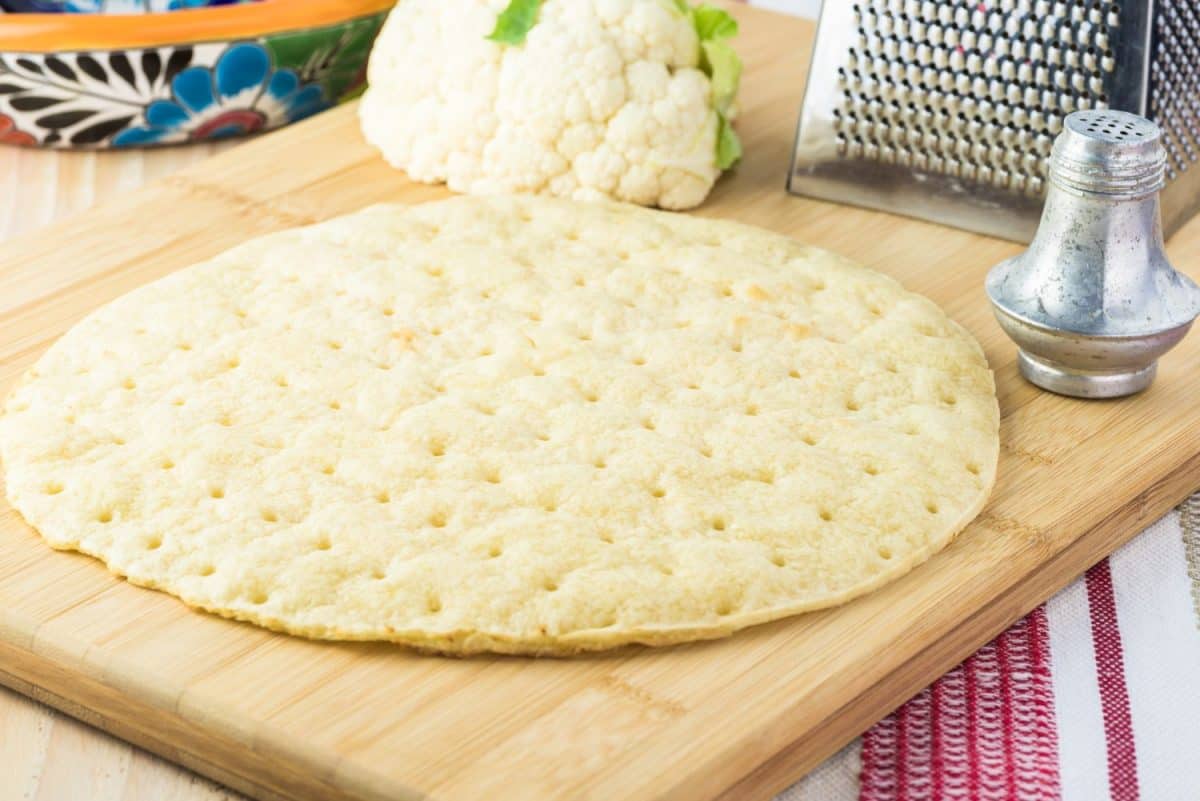 Close up of cauliflower pizza crust on a cutting board.