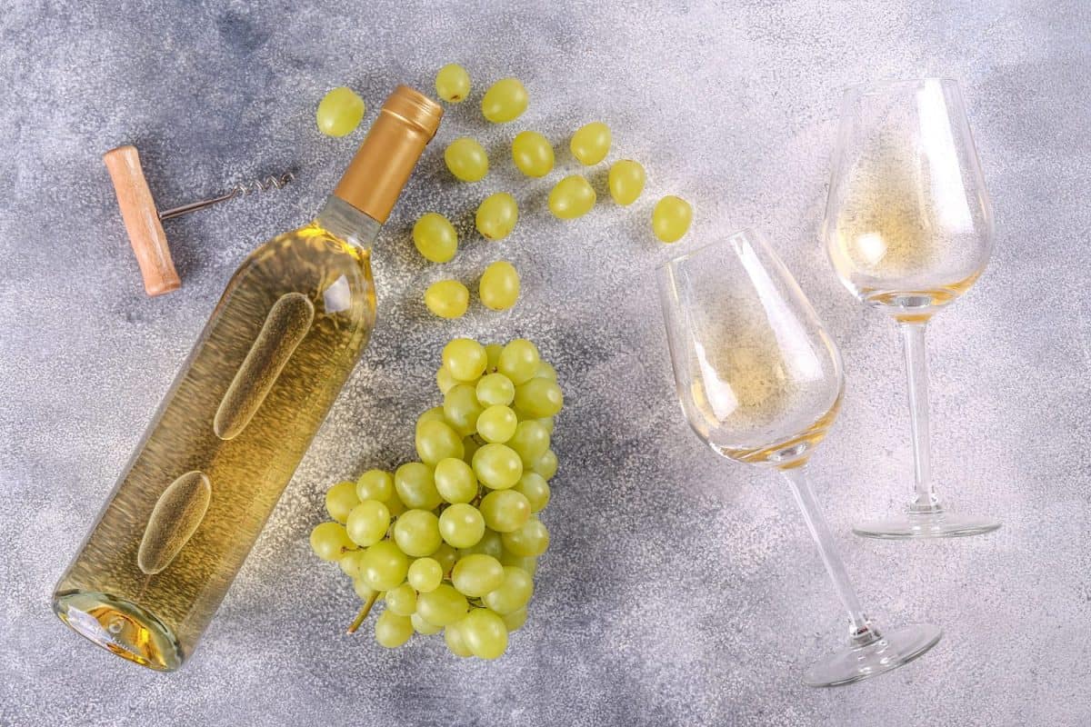 Unopened vintage bottle of white wine without label and bunches of ripe organic grapes on grunged stone table background. Expensive bottle of chardonnay concept. Copy space, top view, flat lay. Forget Chardonnay, These 12 White Wines Are Better