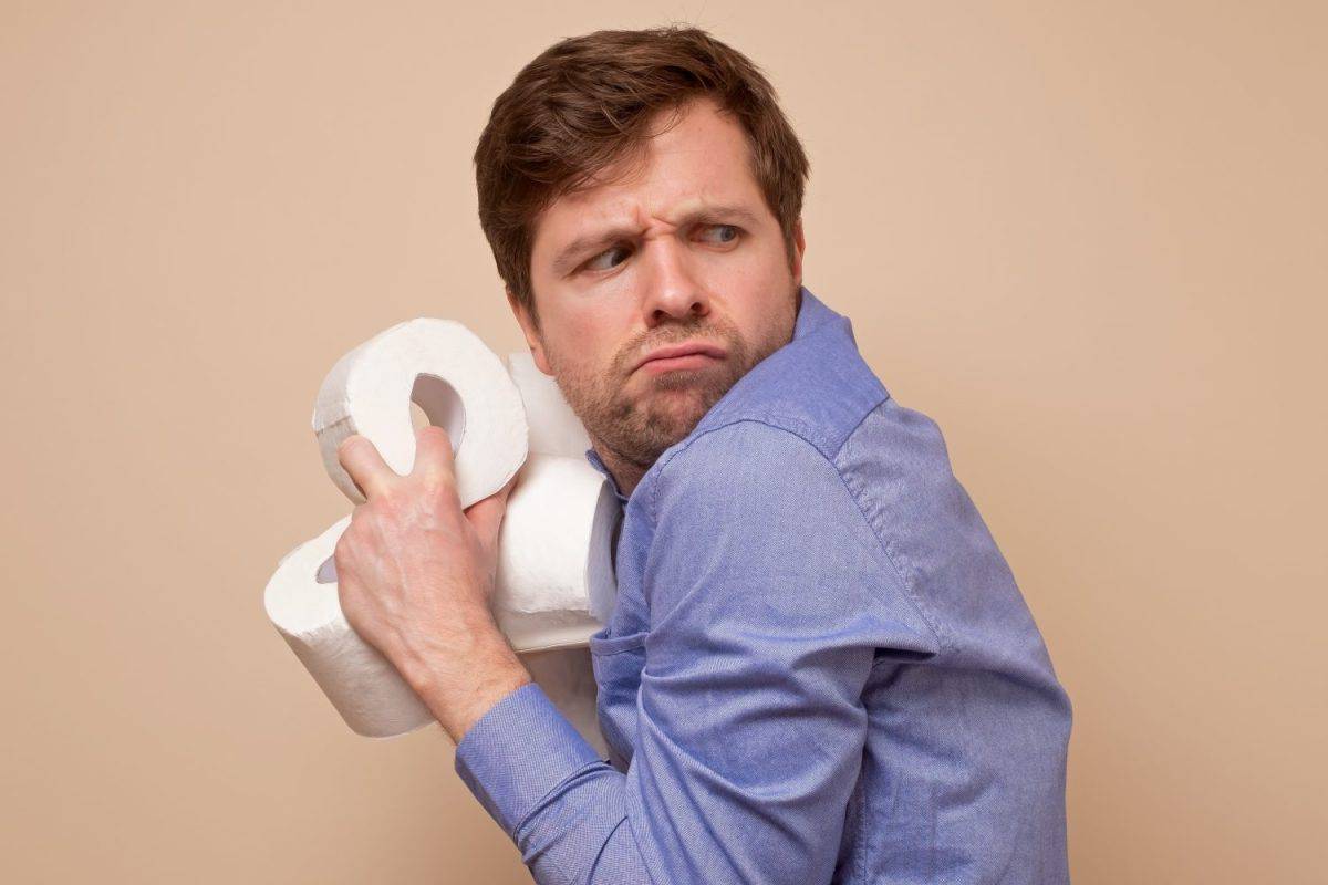 Greedy caucasian man holding several rolls of toiler paper on his hand hiding it from other people. Panic because of coronavirus situation.