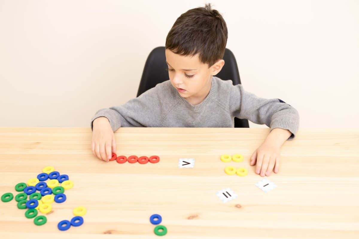 A small preschool child plays a math game, interested, focused. The topic of comparing numbers, concepts of more than, less than, equal to that, smart boy, early home schooling. Caucasian. Copy space.