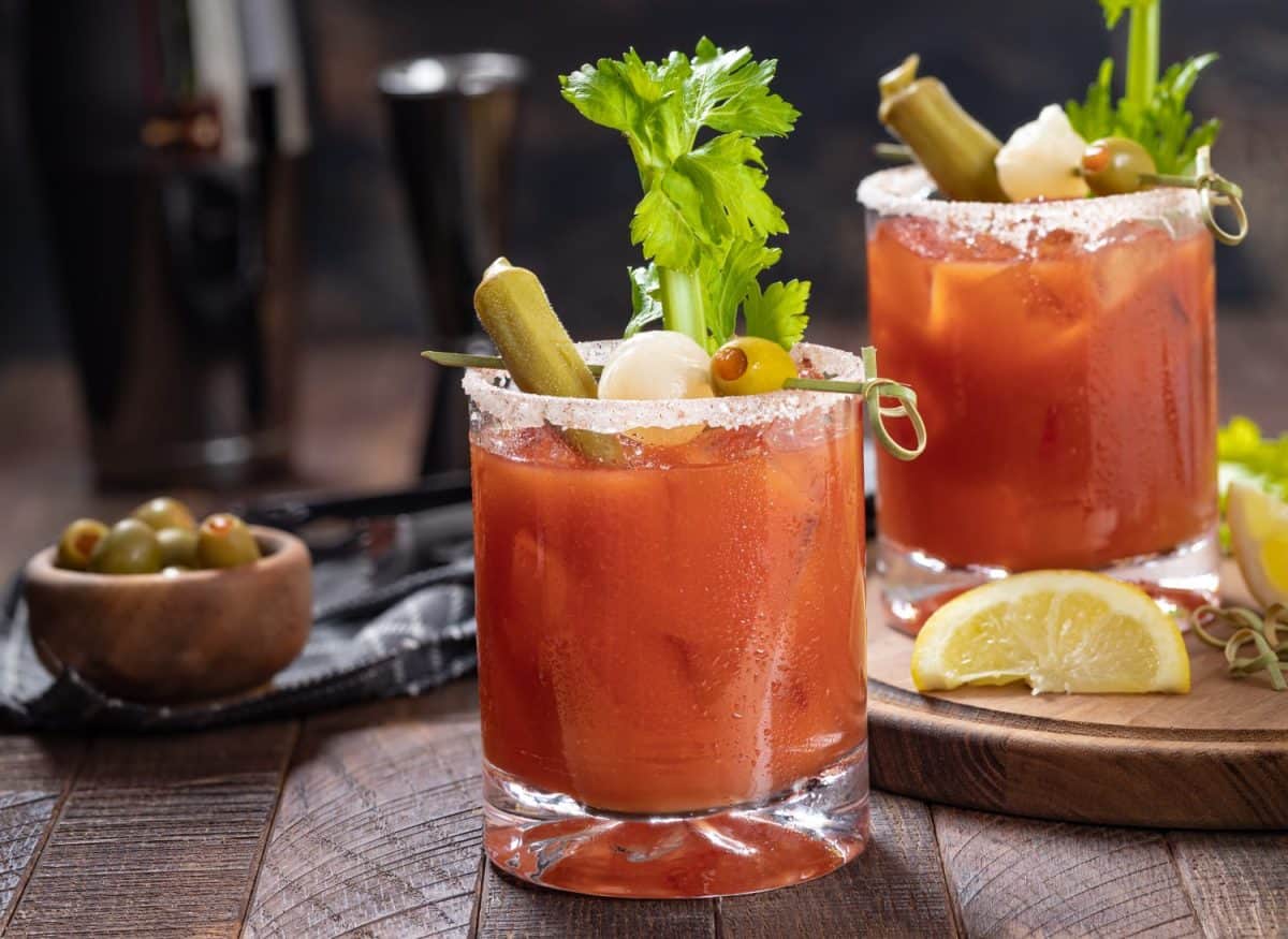 Bloody mary cocktail garnished with celery, okra, onion, olive and salt rim on a rustc wooden table