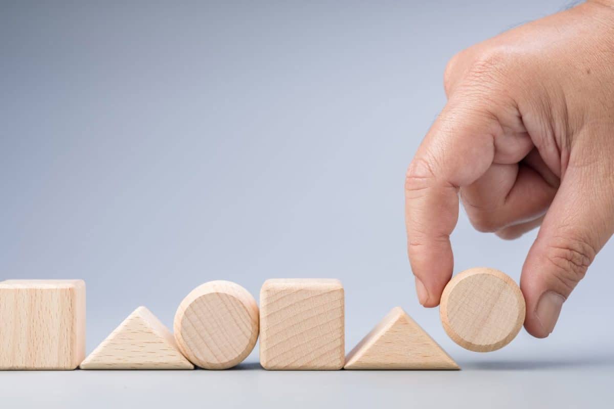 Hand arranges the wooden geometric shape into the same sequence of patterns, logic game, test, and learning