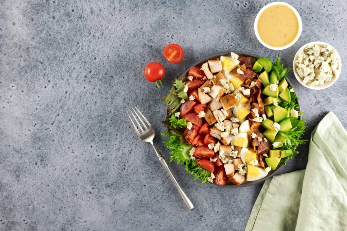 American Cobb salad with tomatoes, bacon, chicken, eggs, avocado, blue cheese on blue background. Top view. Copy space.