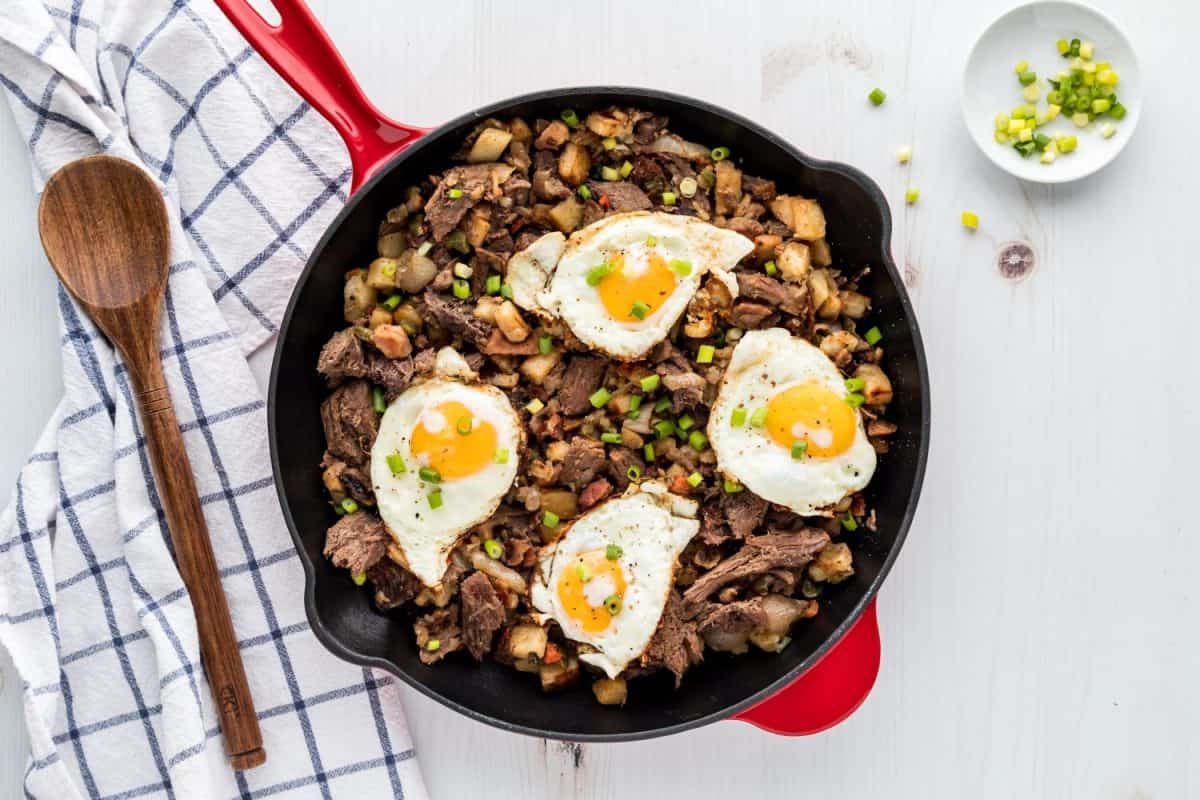 Roast beef hash in a cast iron frying pan topped with fried eggs.