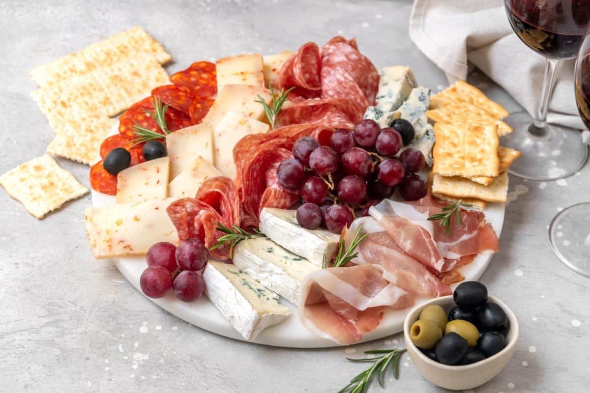 Charcuterie plate with Italian salami and prosciutto ham, with gorgonzrola cheese and pecorino cheese with herbs, served with olives and grapes. Two glasses of wine, appetizer platter for aperitif