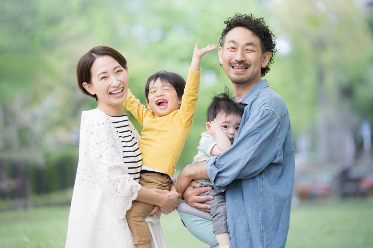 A Japanese family playing together in a fresh green park. They are smiling and looking at the camera in the backlight. This photo was taken from the waist up. Are These Japanese Parenting Tactics Better Than How Americans Raise Children?