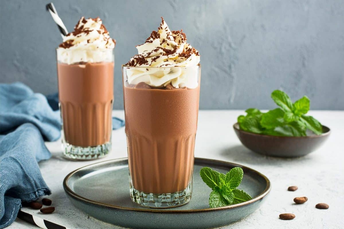 Chocolate milkshake with whipped cream served in glass on table.