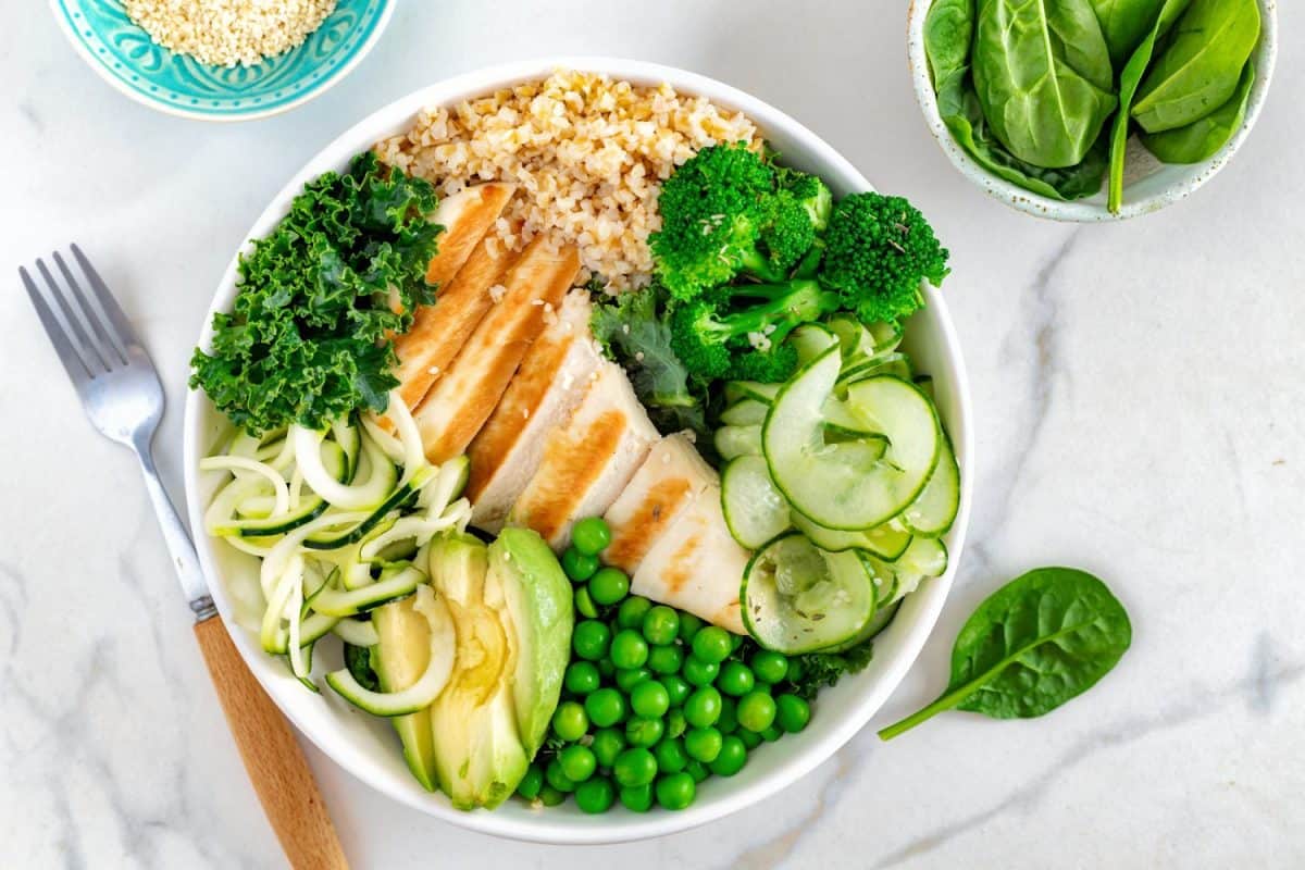 Healthy buddha bowl lunch with grilled chicken, zucchini pasta, green peas, broccoli, cucumber, bulgur grains, spinach and kale, top view