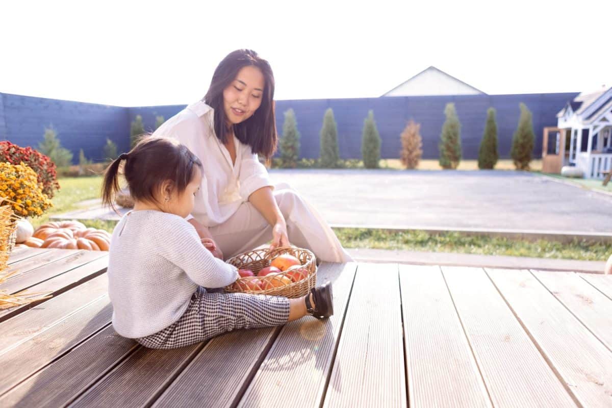 A young Asian woman in white clothes is sitting next to her little daughter. Korean mom and her cute baby in the backyard of the house.