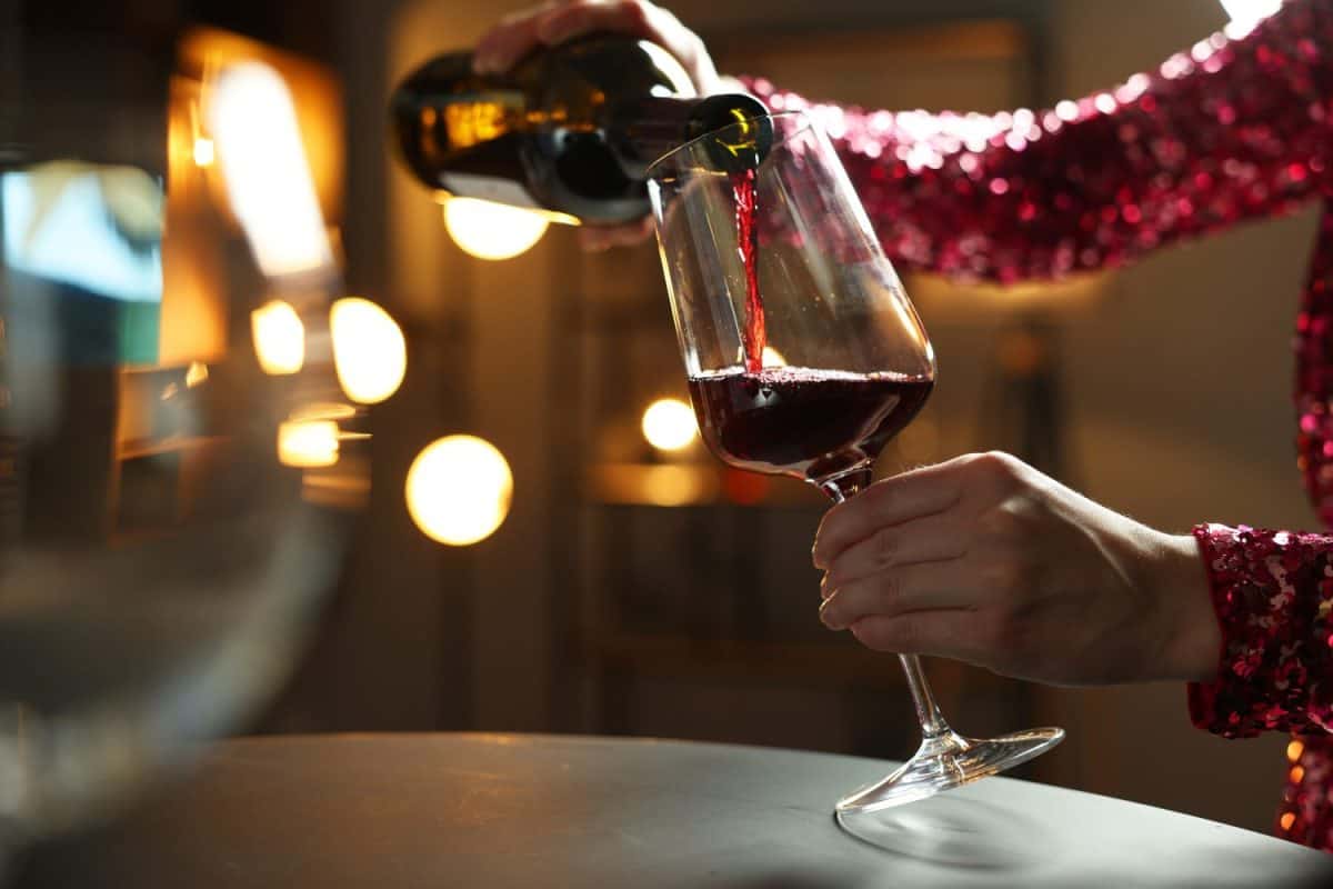 Woman pouring red wine from bottle into glass at table indoors, closeup. I Used to Only Drink Cabernet Sauvignon, But These 16 Red Wines Are Better