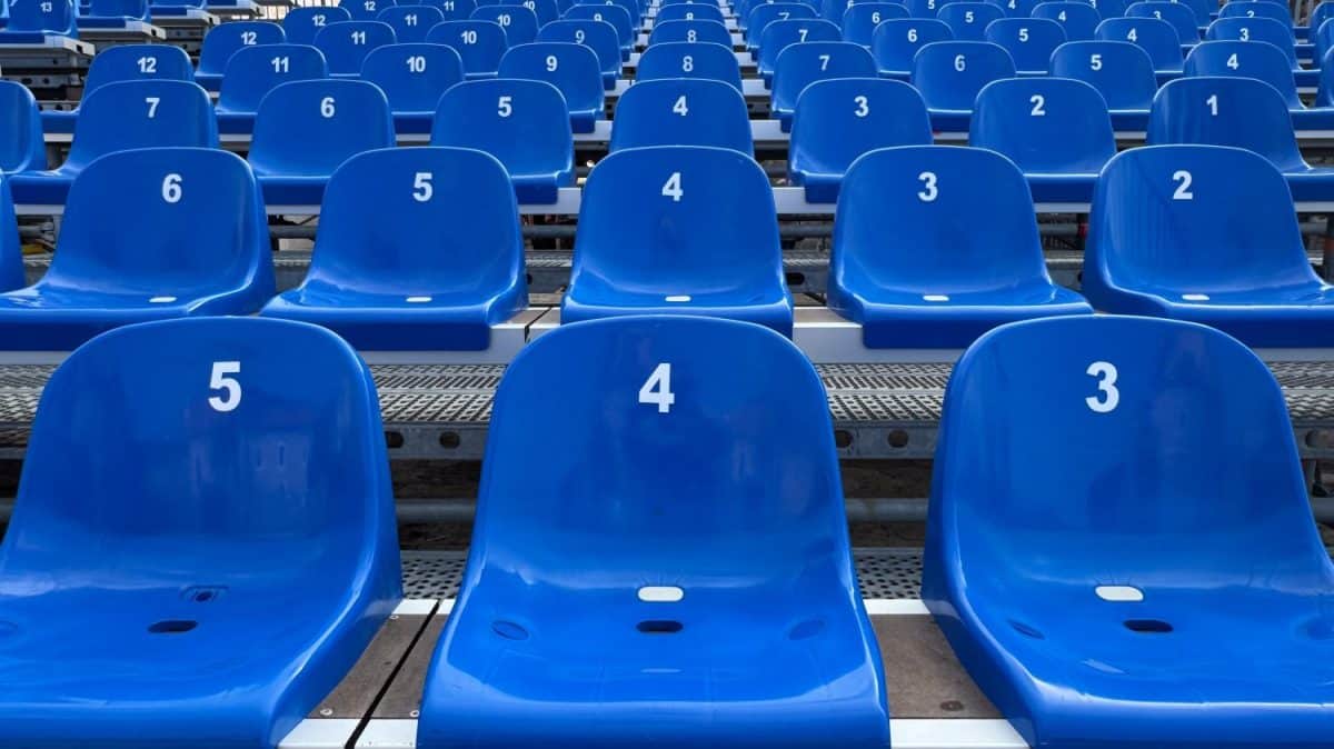 Multiple rows of empty blue stadium seats, each labeled with white numbers, lined up symmetrically, creating a repetitive pattern. The scene is orderly and structured.