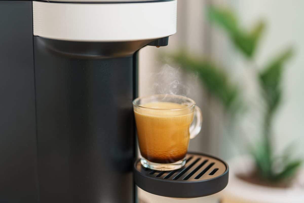 Espresso cup with steam and froth during Coffee making Coffee by Coffee Maker Machine on wood table bar. Cafe shop, Daily beverage drink at Home, Apartment and Office concept