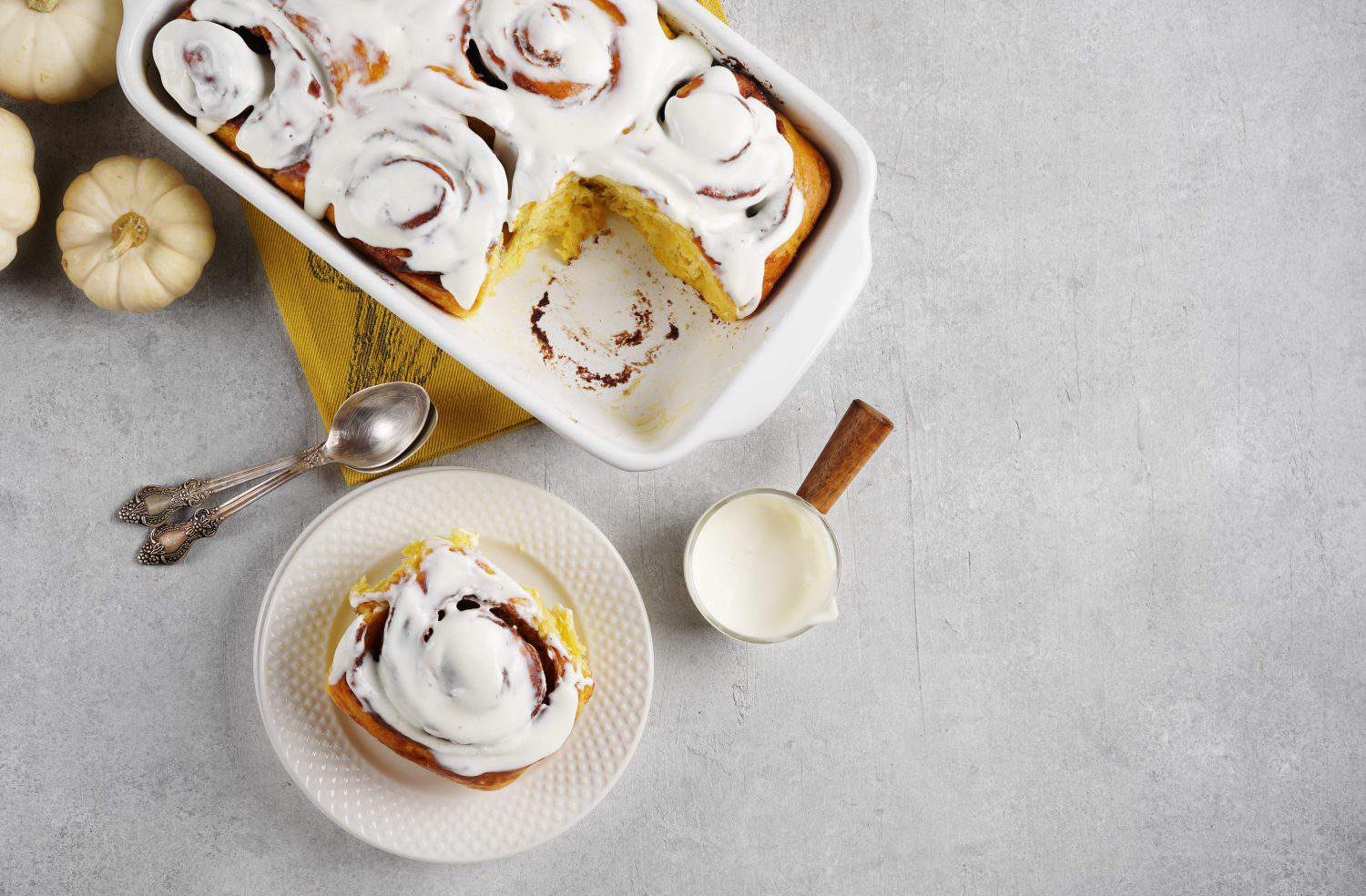 Fragrant freshly baked Cinnamon rolls or cinnabons with pumpkin covered with white cream glaze on the plates on white background. Cinnabons recipe. top view, copy space