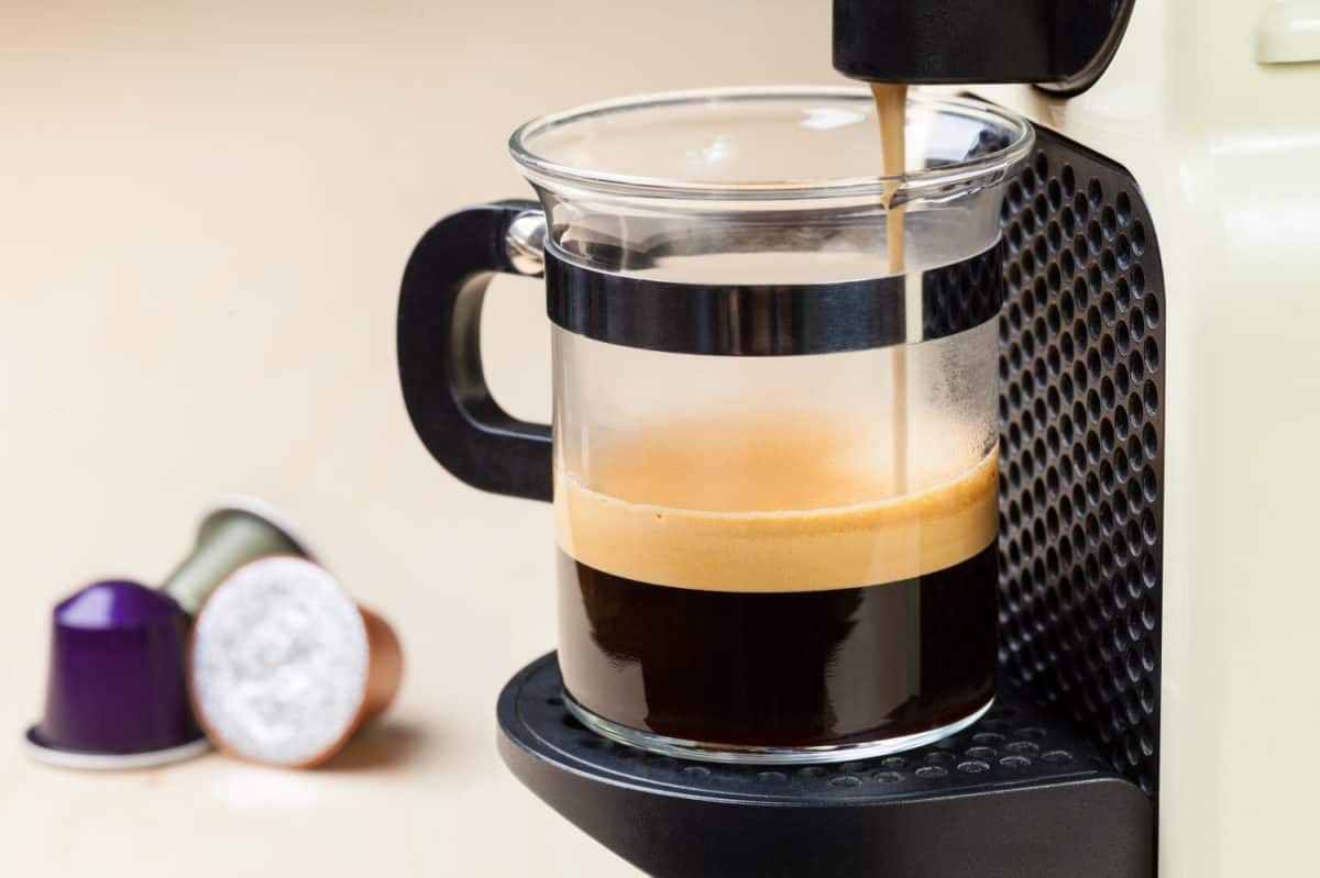 Single-serving coffee machine dispenses espresso in a glass cup with coffee capsules in background