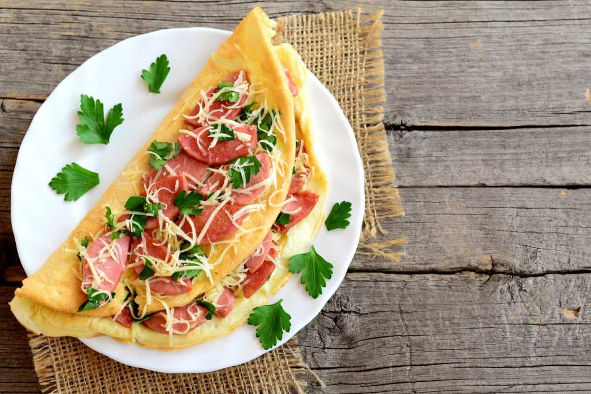 Delicious sausage and cheese omelette on a plate and an old wooden background with blank copy space for text. Eggs omelette with a filling. Vintage style. Top view