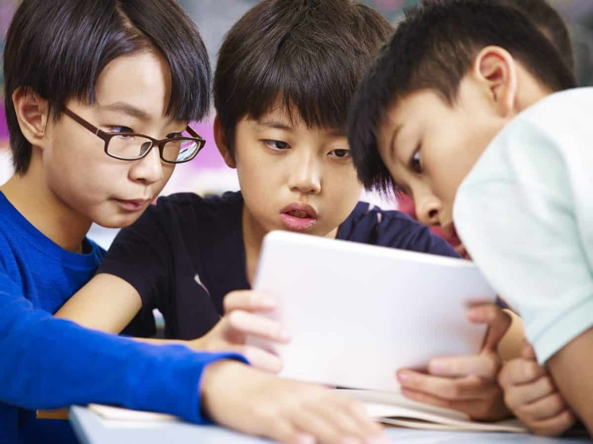 three asian primary school student playing video game using tablet computer with serious facial expression.