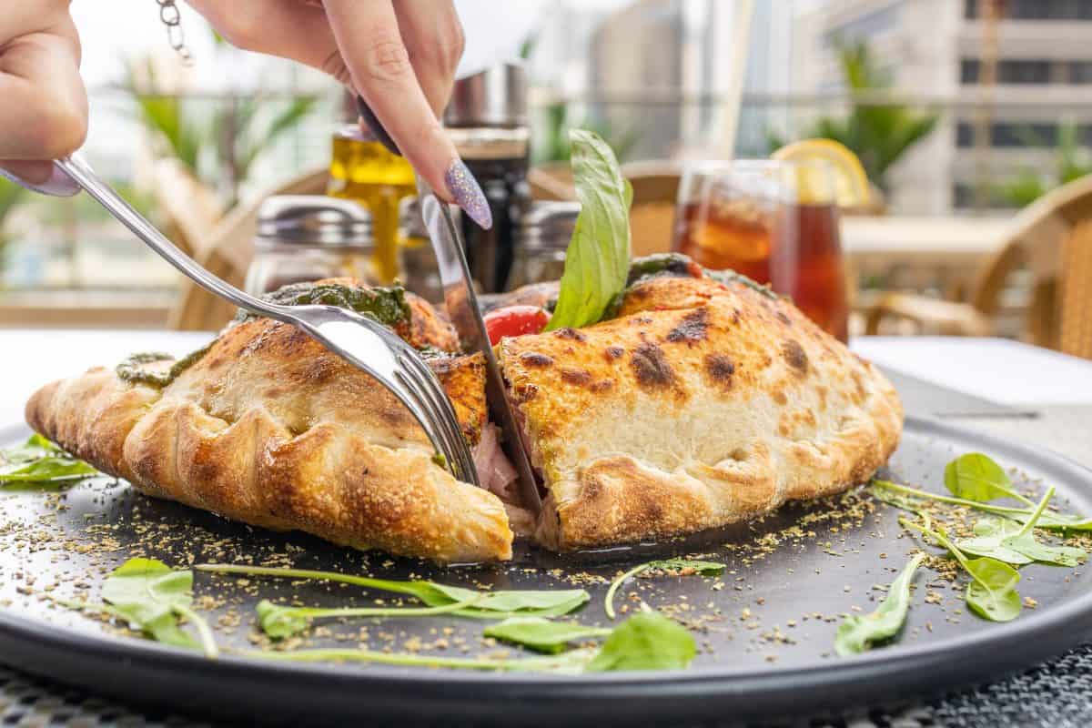 Pizza calzone with basil leaves close up with restaurant background. classic italian food