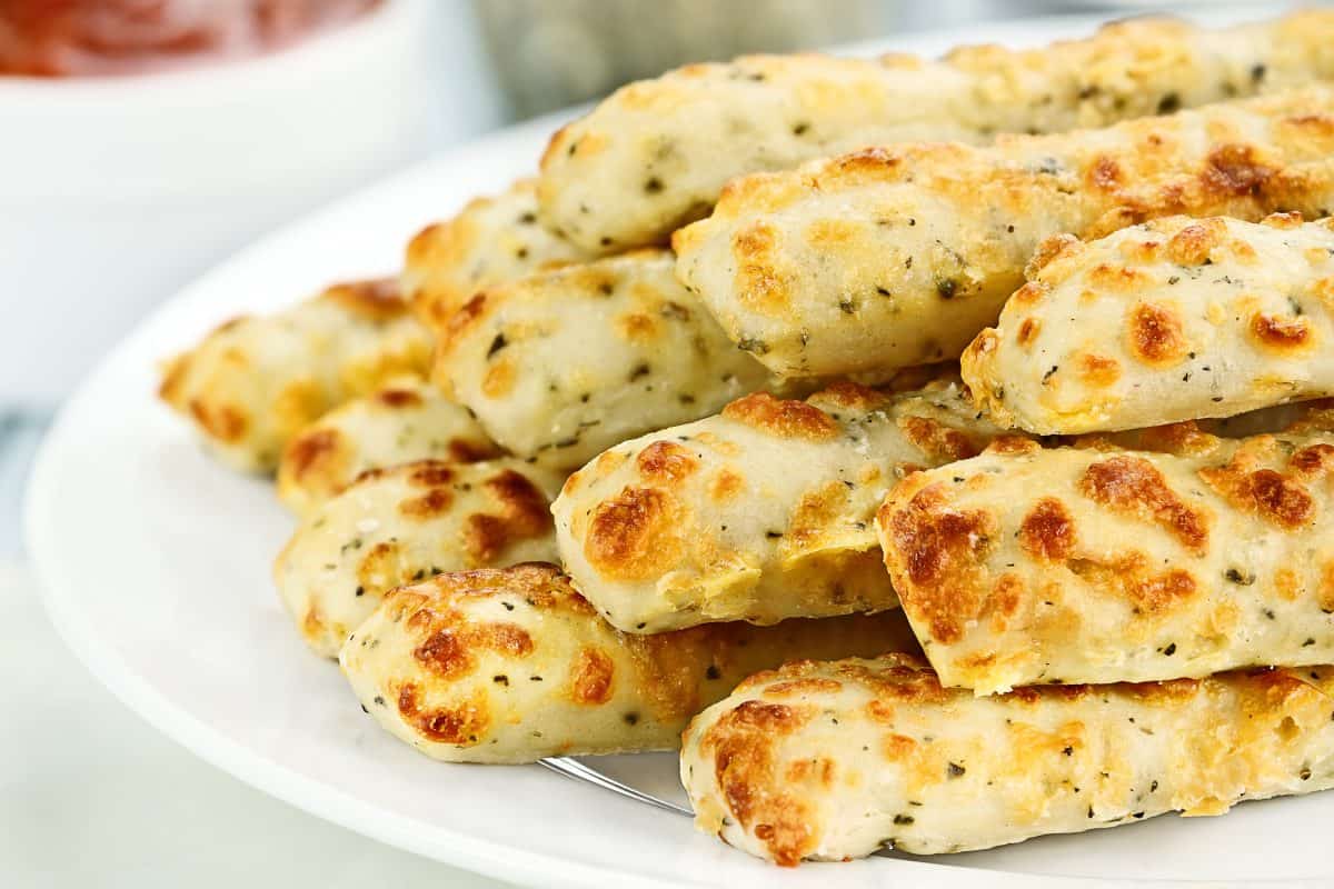 Fresh golden, cheesy breadsticks with marinara sauce and parmesan cheese in background. Shallow depth of field.