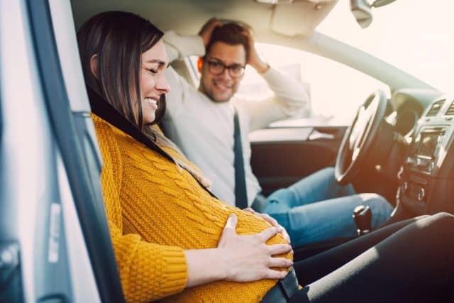 Pregnant woman starting to feel pain and contractions while her worried husband driving a car. She is ready to give birth in a car.