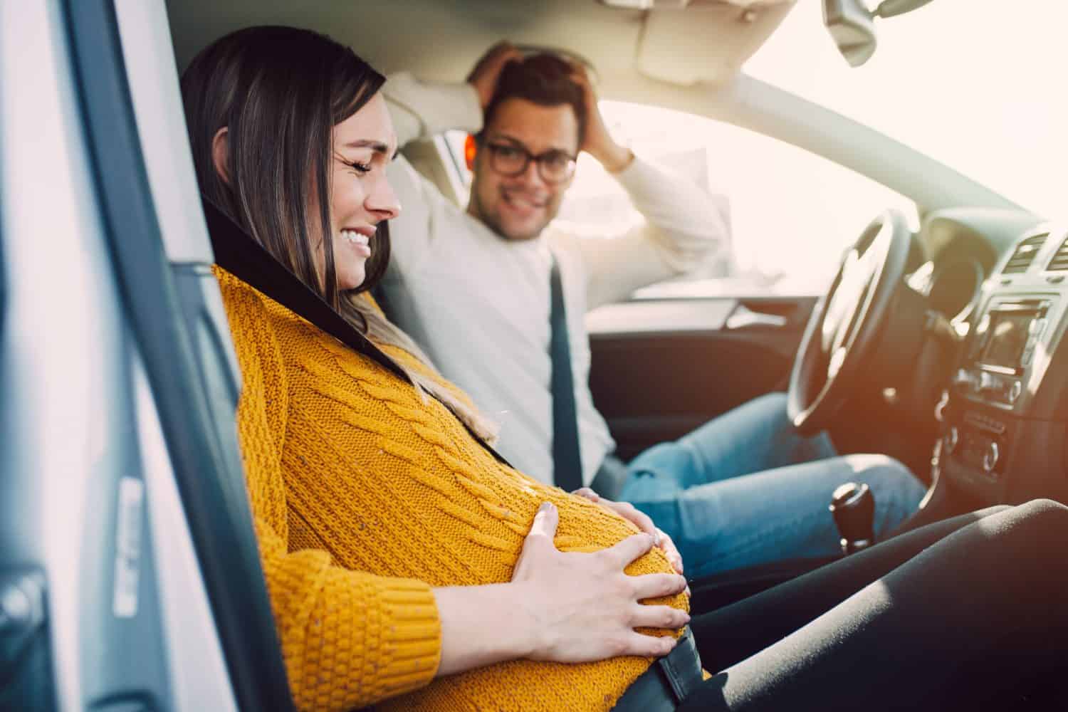 Pregnant woman starting to feel pain and contractions while her worried husband driving a car. She is ready to give birth in a car.