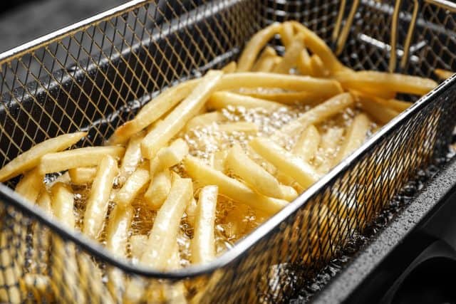 Cooking delicious french fries in hot oil, closeup