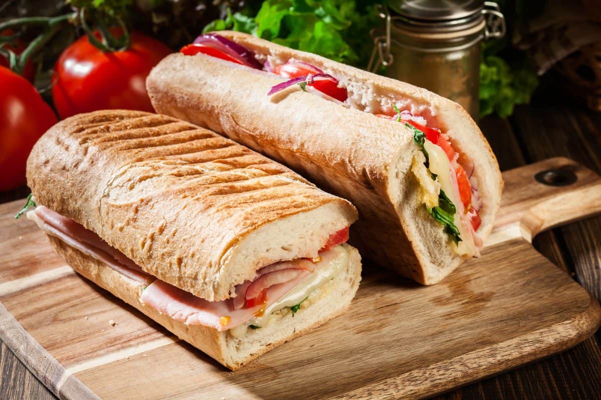 Toasted panini with ham, cheese and arugula sandwich on cutting board