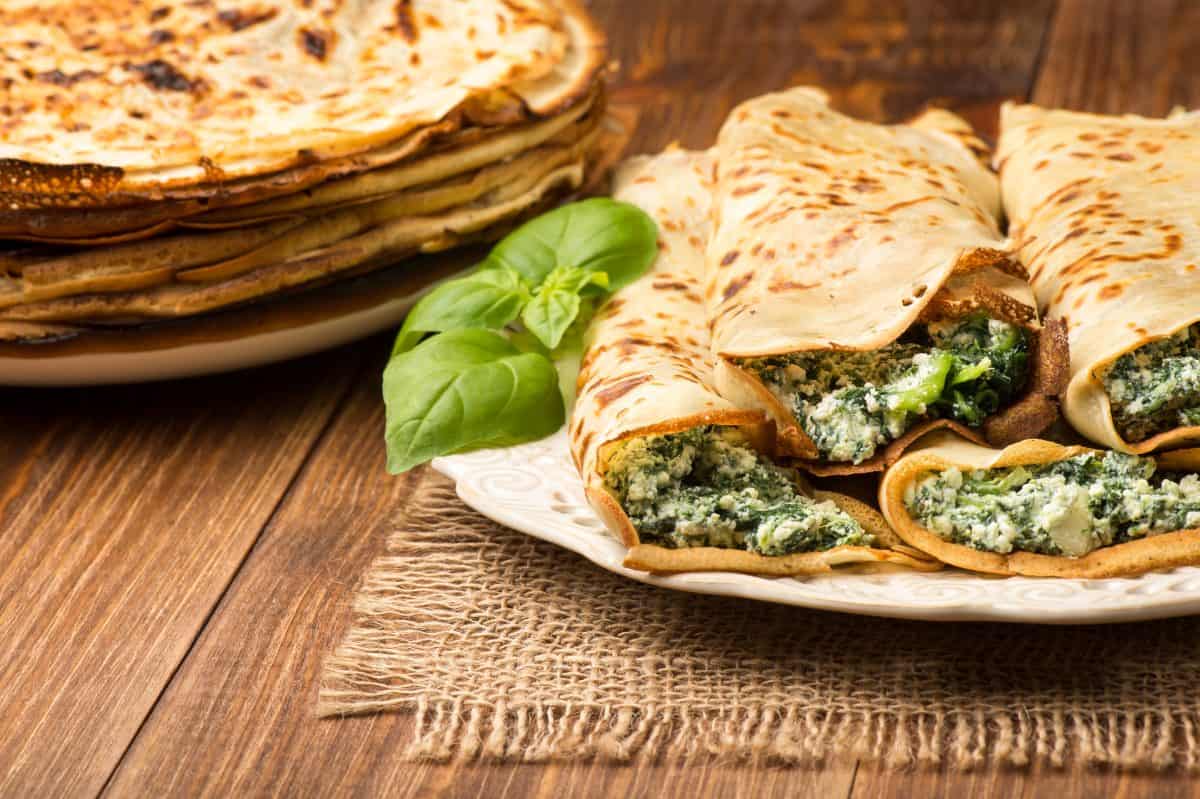 Pancakes filled with spinach and cheese on the wooden surface.