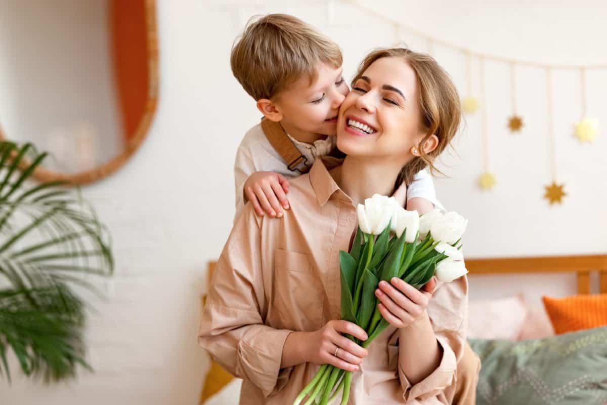 tender son kisses the happy mother and gives her a bouquet of tulips, congratulating her on mother's day during holiday celebration at home