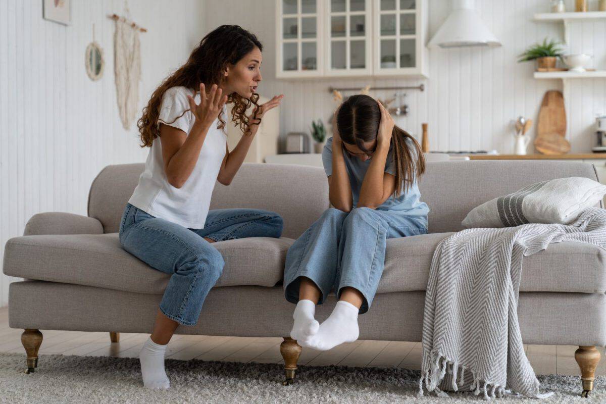 Angry mad mother trying to discipline child, expressing frustration shouting at teenage daughter sitting on sofa covering ears with hands. Psychological effects of yelling at kids, verbal abuse