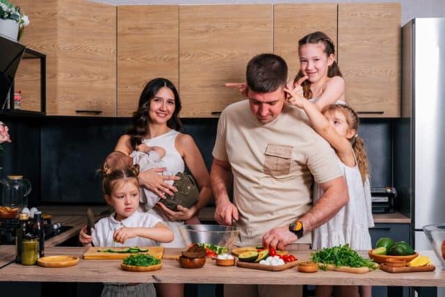 A large family - mom, dad, three daughters and a baby son together prepare a salad for lunch in a modern kitchen. Big family together concept.